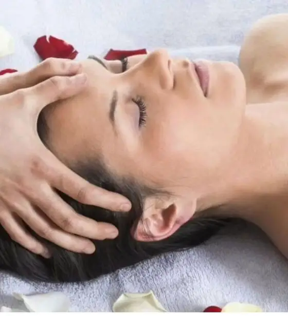 A client relaxing with eyes closed during a gentle head massage, rose petals around her